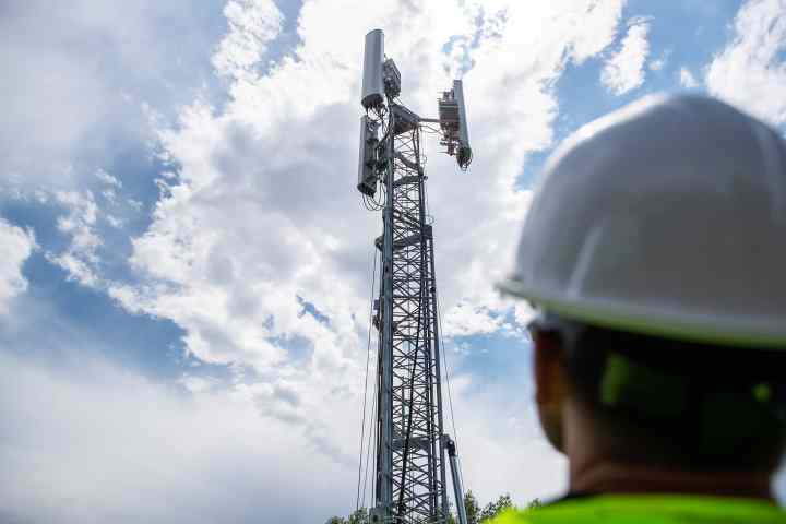 عامل ينظر إلى برج 5G مقابل سماء ملبدة بالغيوم.