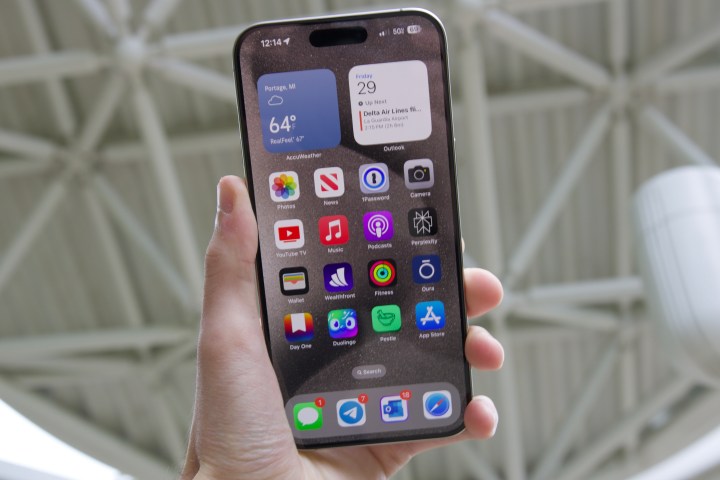 شخص يحمل هاتف iPhone 15 Pro Max في الخارج.